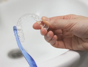 Hands cleaning Invisalign with blue toothbrush