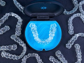 Bird’s eye view of several Invisalign trays around a carrying case on black surface