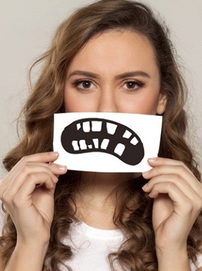 A woman holding a picture of a damaged smile over her mouth.