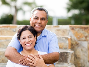 An older couple smiling and hugging outside.