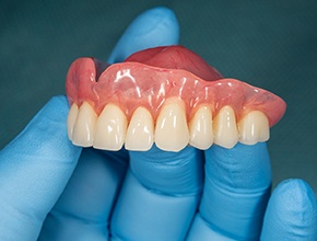 A gloved hand holding a removable upper denture