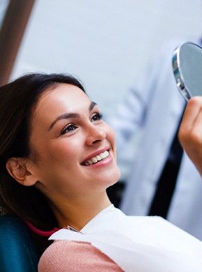 Young woman looking at new dental implants in handheld mirror