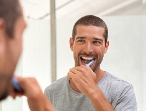 Man smiling and brushing his teeth in mirror