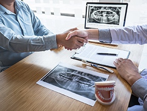 Dentist and patient shaking hands over desk