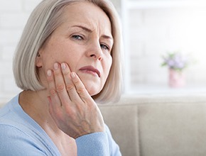 Woman with dental implants in Manchester, NH rubbing jaw looking concerned