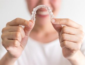Smiling patient holding aligners after paying for Invisalign in Manchester 
