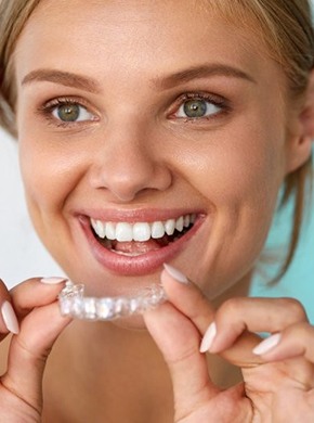 A woman smiling and holding a clear aligner.