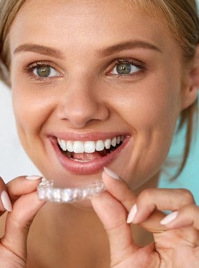 A woman smiling and holding a clear aligner.