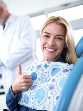 smiling woman giving a thumbs up in the dental chair 