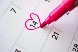 person drawing a heart around the date February 14th on a calendar