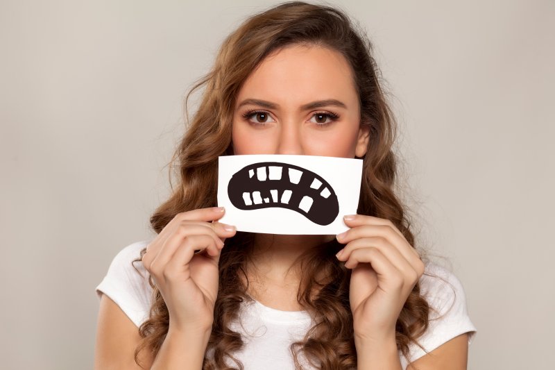 Woman holding signage of bad teeth in front of her mouth