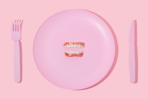Set of dentures on a pink plastic plate with pink fork and knife on either side