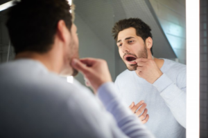 Man pulling his lip back to examine his dental crown in a mirror